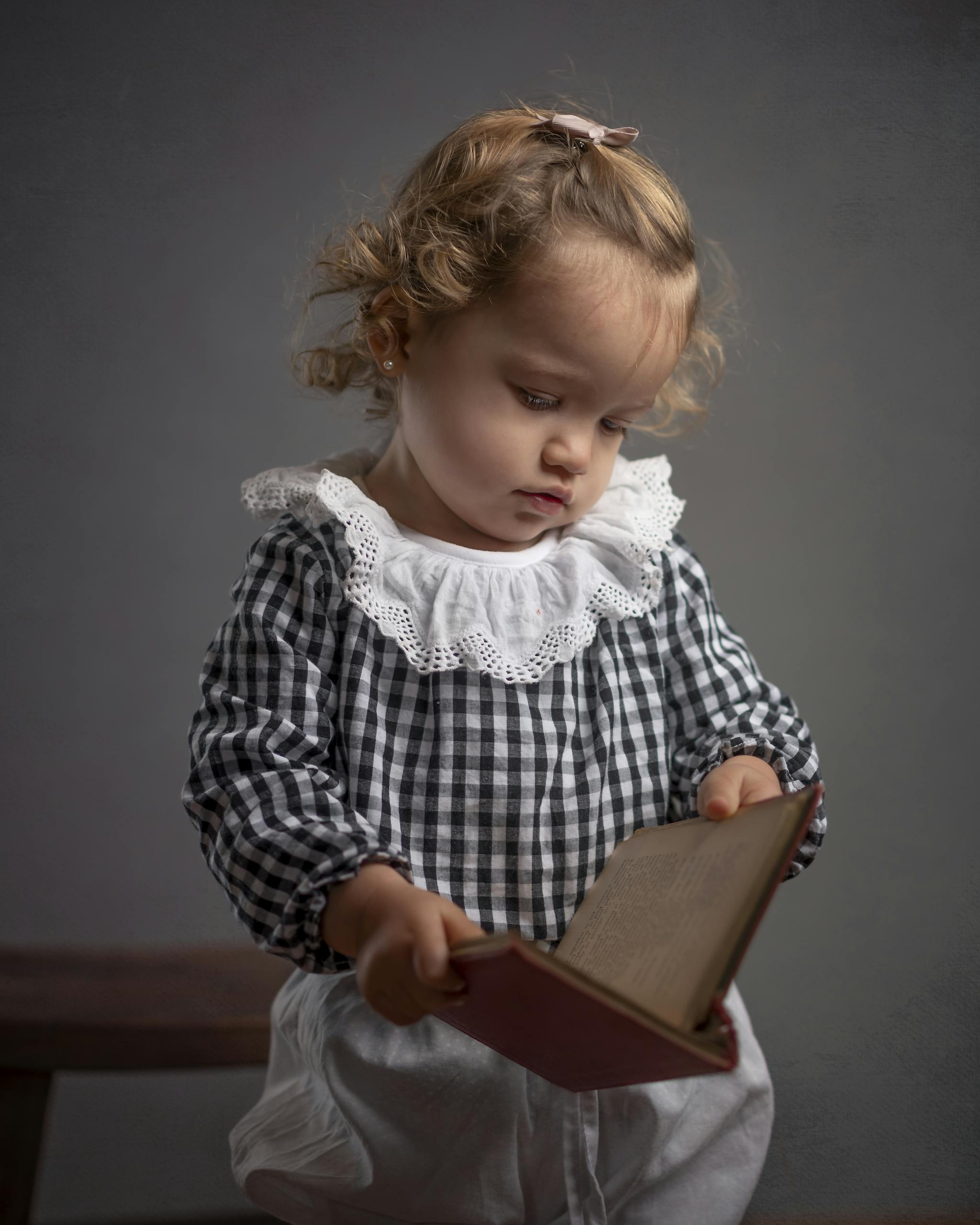 Adorable child in checkered outfit reading a book, showcasing curiosity and innocence.