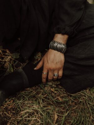 Close-up of a hand with silver jewelry against earthy grass background, conveying elegance.