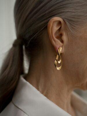 Close-up of senior woman with gray hair, showcasing elegant gold earrings and fashion style.