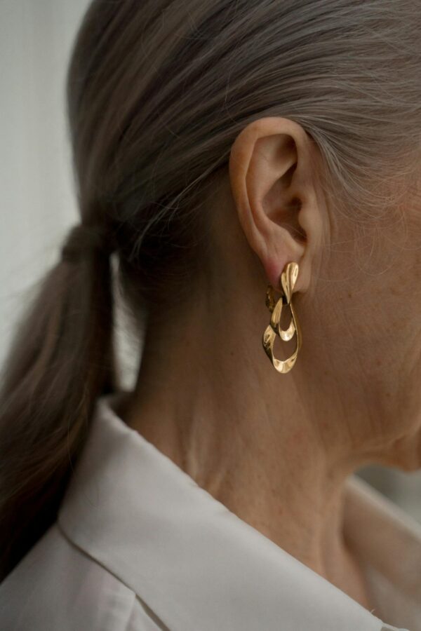 Close-up of senior woman with gray hair, showcasing elegant gold earrings and fashion style.