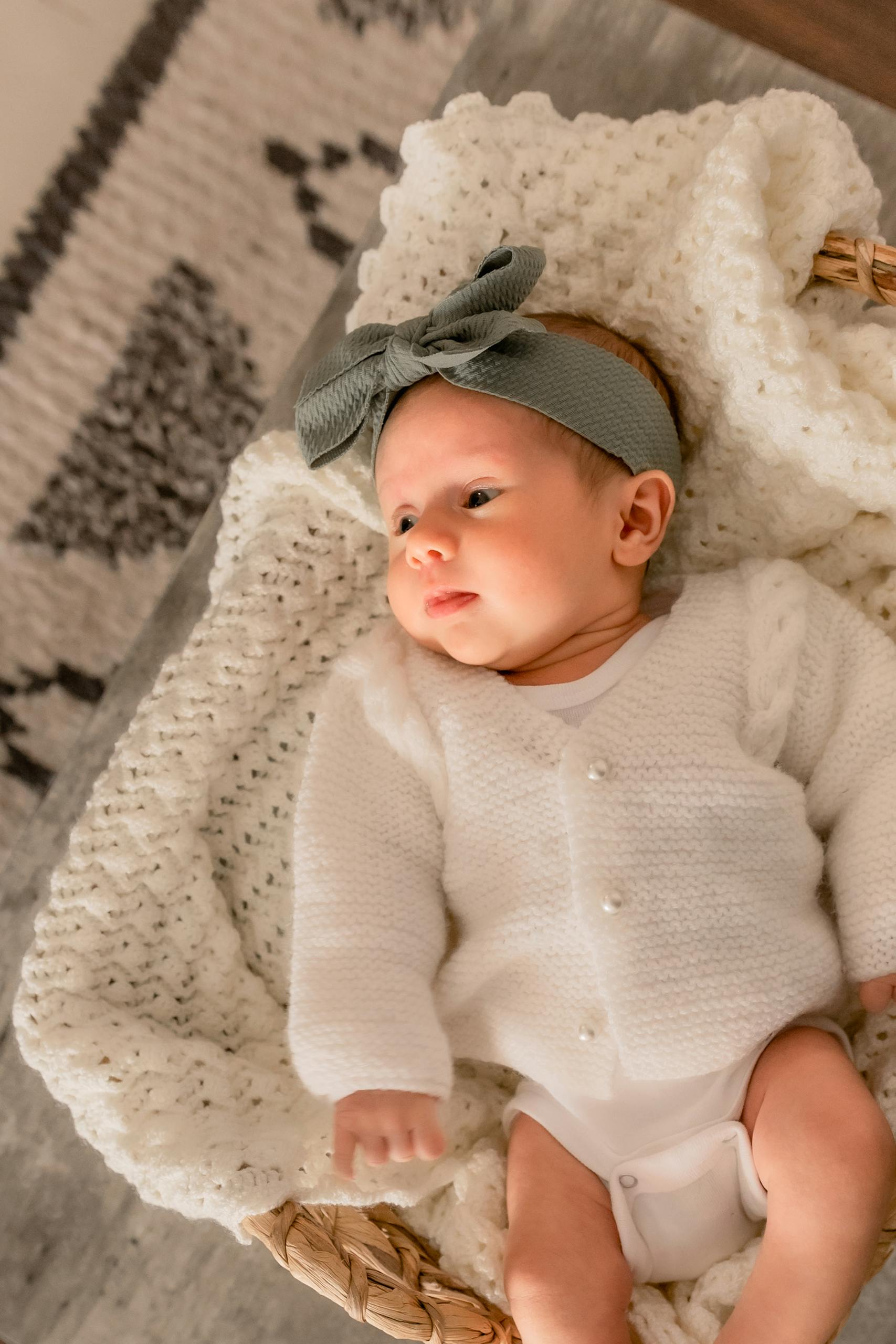 Sweet baby girl in white knitwear lying in a cozy basket, exuding innocence and cuteness.