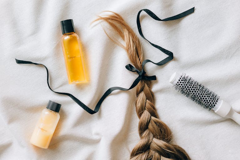 Flat lay of braided hair with shampoo bottles and brush on white fabric, conveying beauty and haircare themes.