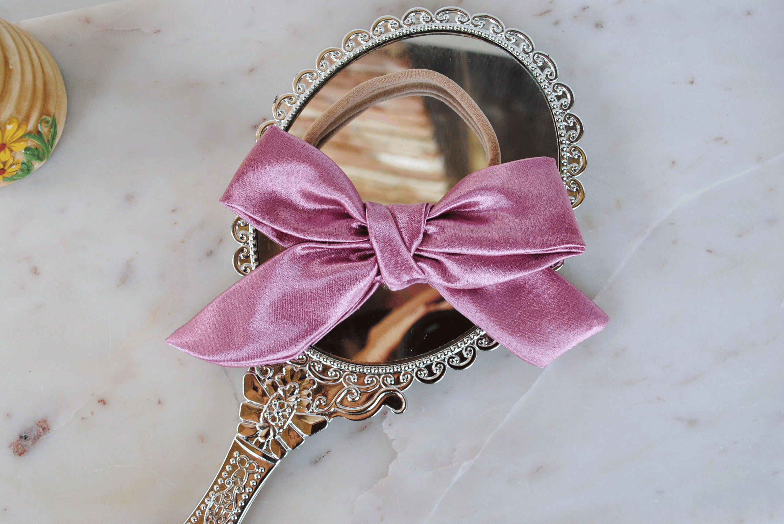 a luxe baby headband in rose pink satin on a marble top
