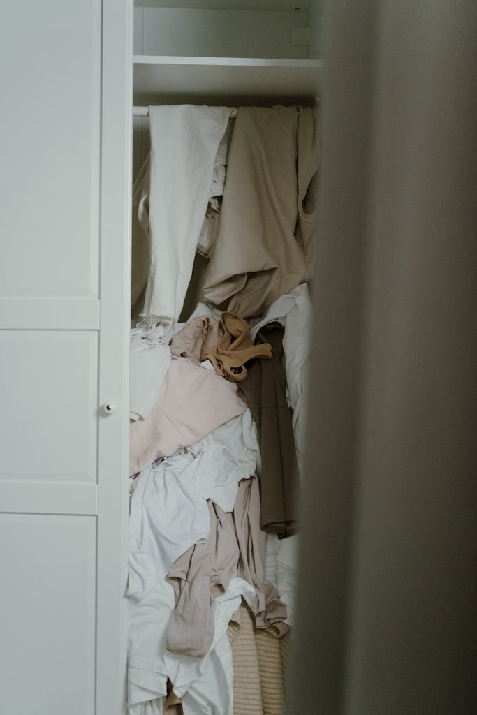 A cluttered wardrobe with clothes haphazardly hanging and stacked, showcasing disorder.
