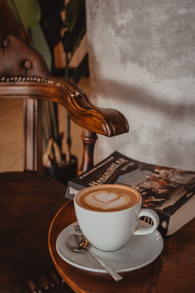 Warm cafe setting with cappuccino and book on a wooden table, ideal for relaxation themes.