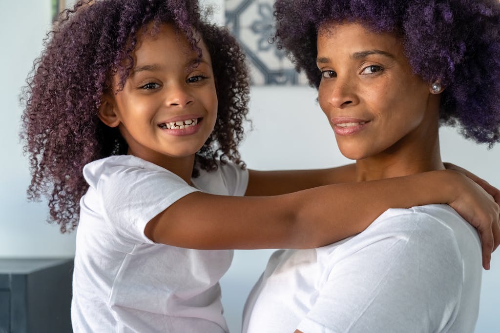 Protective Styles for Curly Kids: Low-Tension Looks That Stay Put 3 Joyful mother and daughter sharing a warm embrace indoors, highlighting family love and connection.