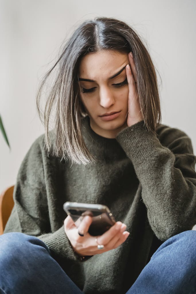 What We Lose When We Rush Girlhood: A Mother's Manifesto 7 Unhappy female in casual wear leaning on hand and surfing internet on cellphone while sitting in light room near wall at home
